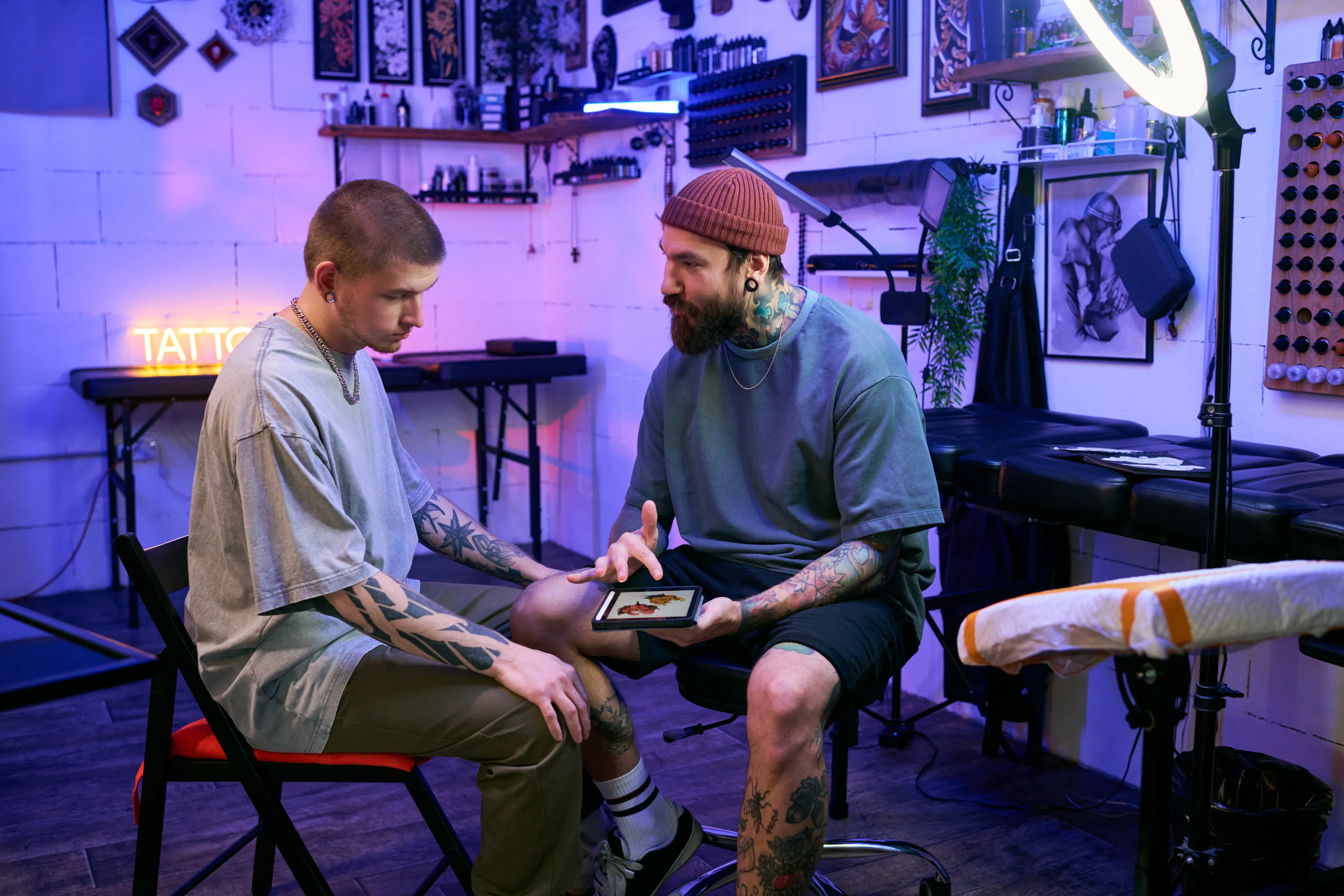 Tätowierer zeigt Kunden Buchungsübersicht auf einem Tablet im Tattoostudio